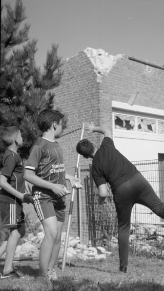 Three young boys in front of an empty building building. One throws a rock towards it.